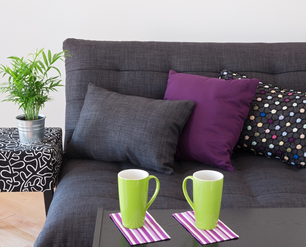sofa decorated with bright cushions, green plant and big cups on a table.
